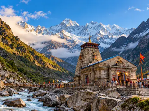 Stone temple at the foot of snow-covered Himalayan peaks beside a mountain river.